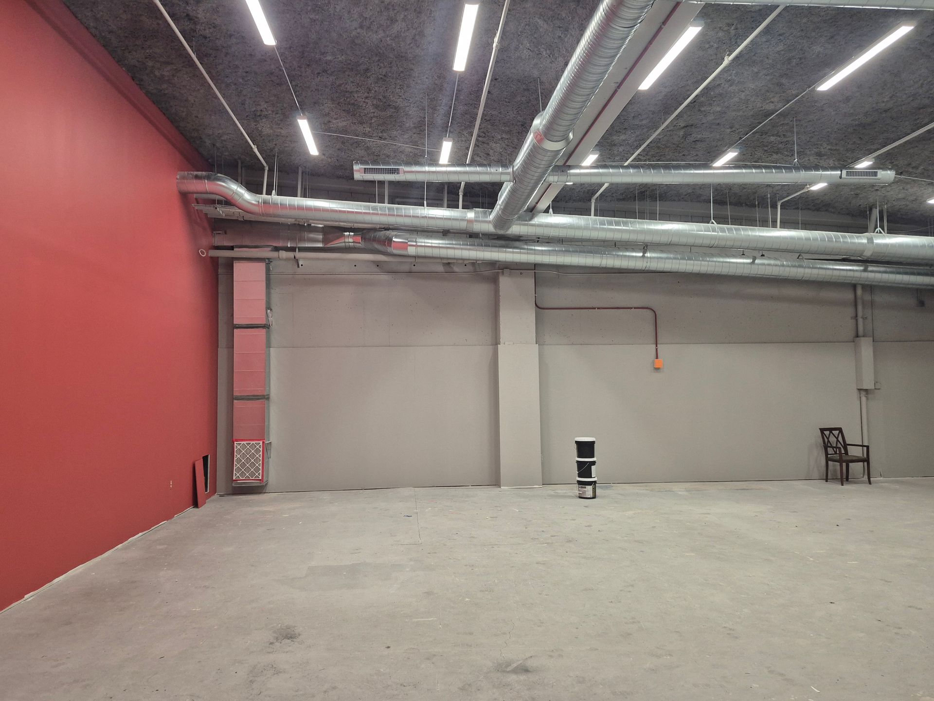 A large empty room with a red wall and a chair.