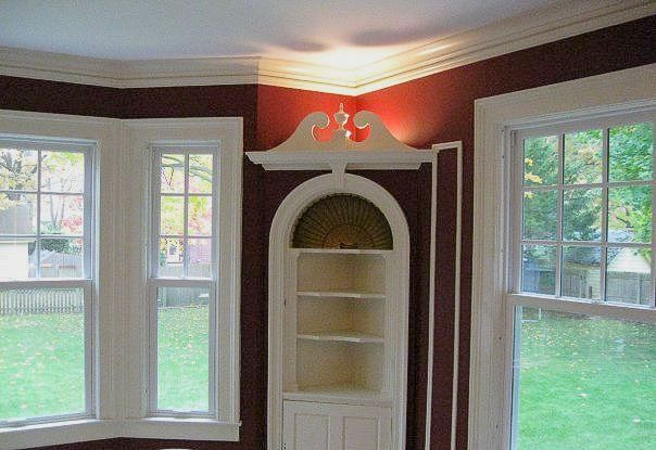 A corner of a room with a shelf and two windows