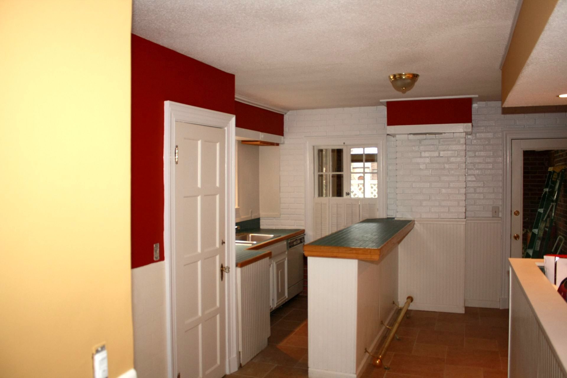 An empty kitchen with red walls and white cabinets