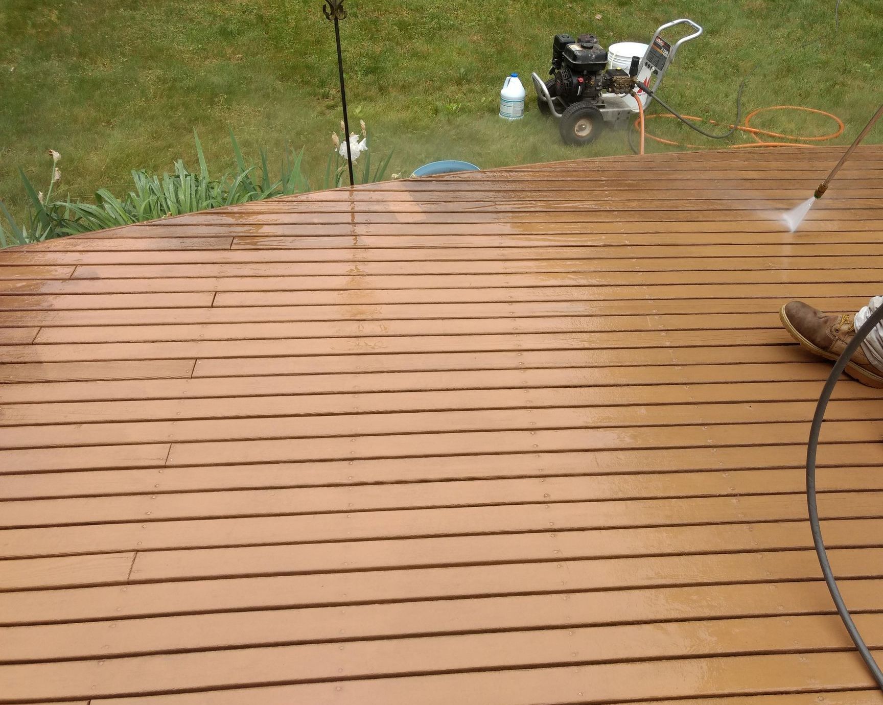 A person is cleaning a wooden deck with a pressure washer.