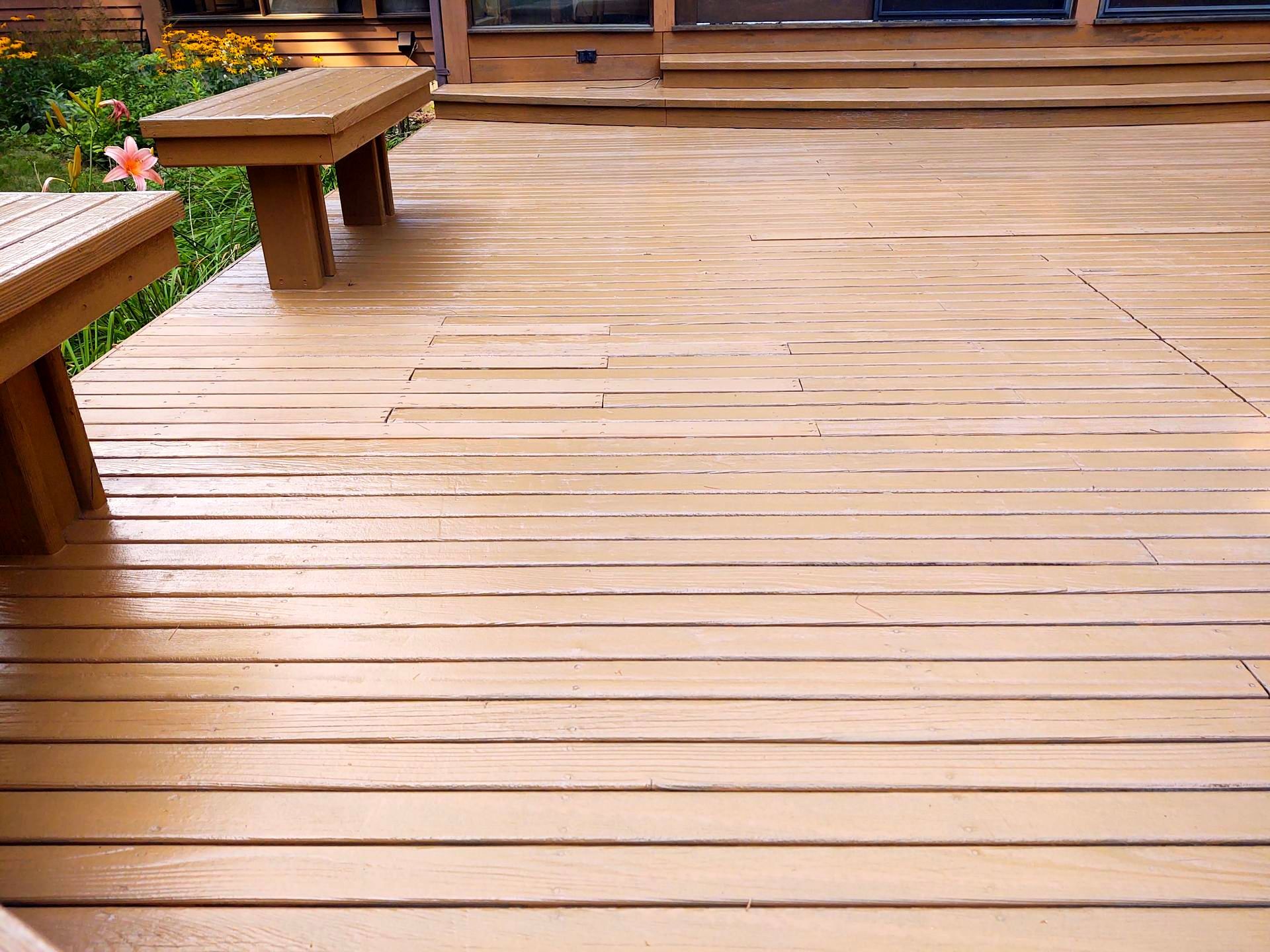 A wooden deck with a bench and flowers in the background