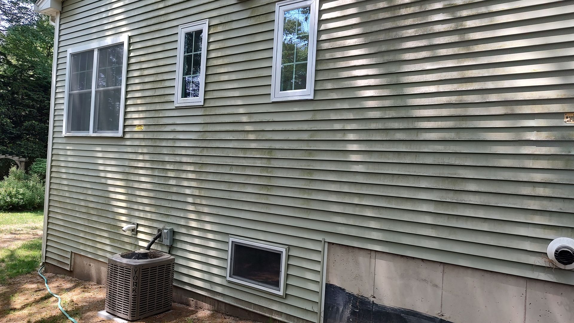 The side of a house with a green siding and white windows.