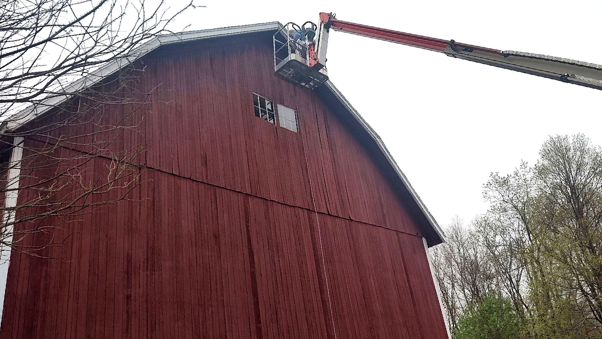 A man is cleaning the roof of a red barn with a crane.