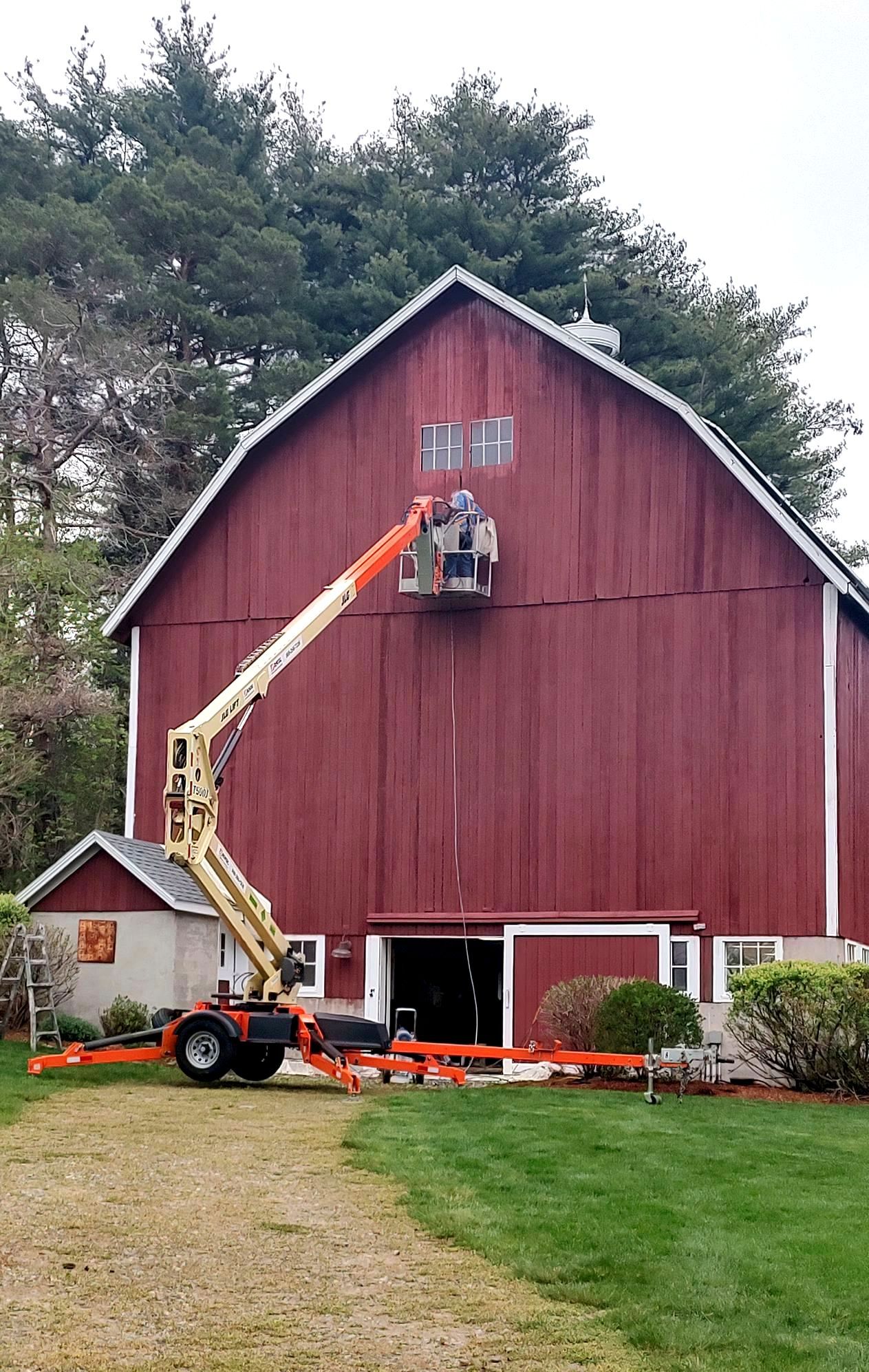 A man is painting a red barn with a crane.