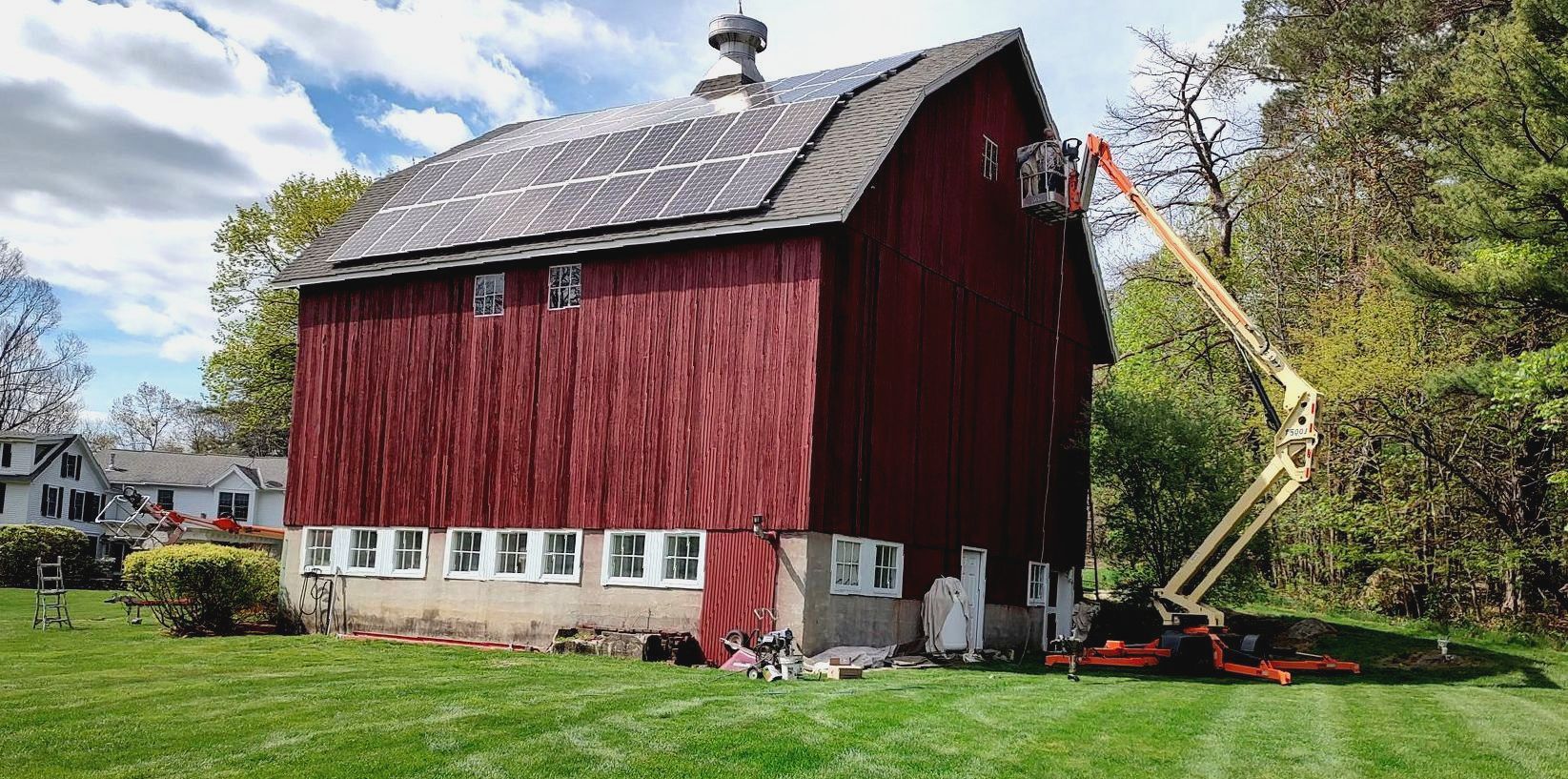 A red barn is being painted with a crane.