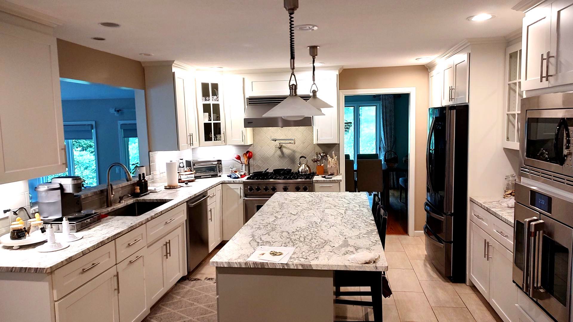 A kitchen with white cabinets , granite counter tops , stainless steel appliances and a large island.