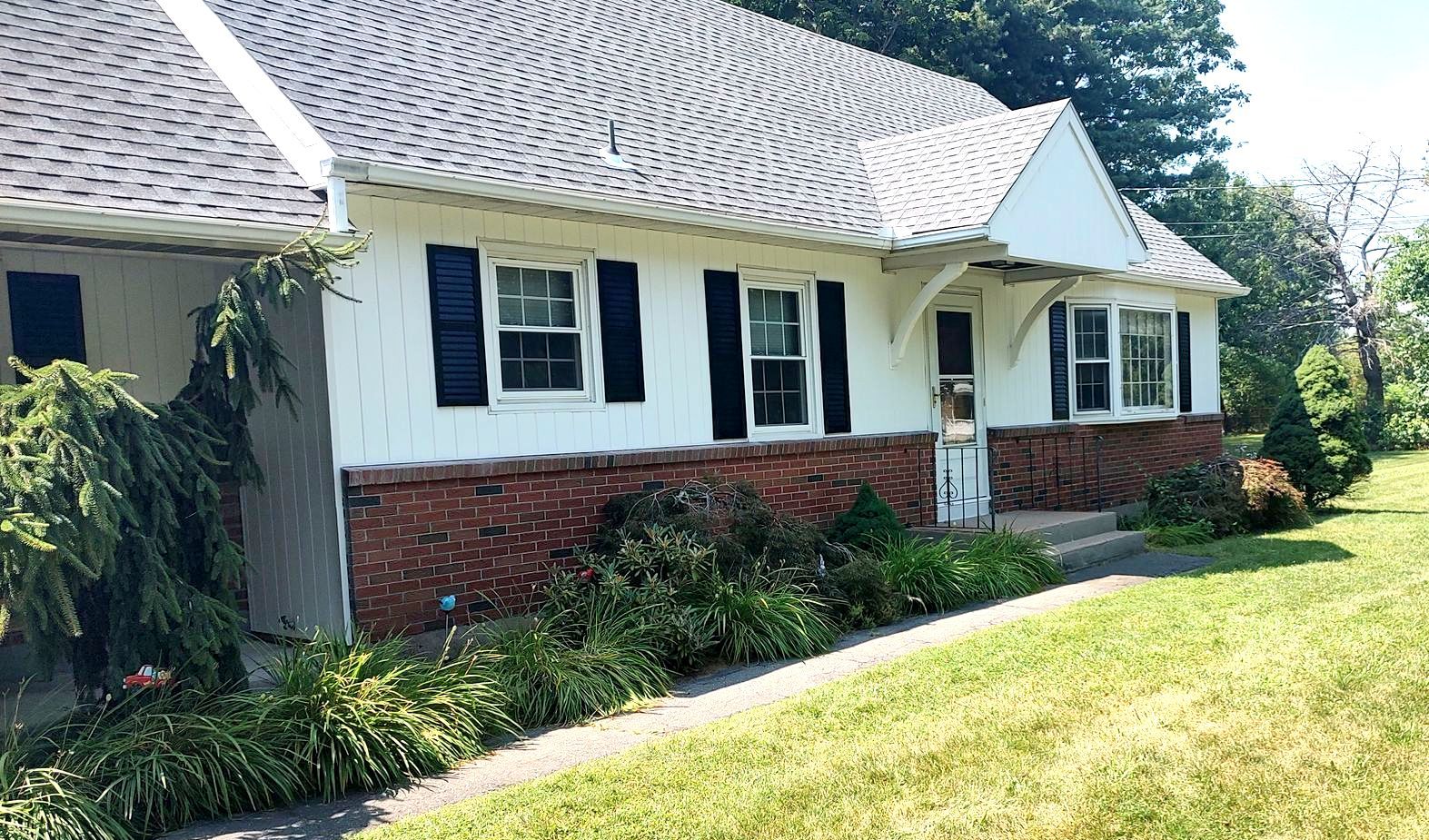 A white house with black shutters is sitting on top of a lush green field.