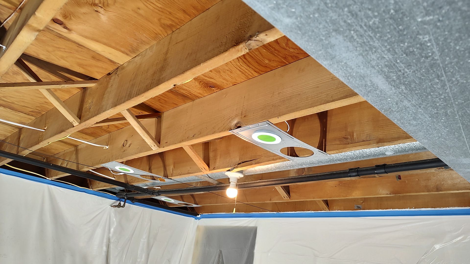 The ceiling of a basement is being remodeled and there is a light on the ceiling.
