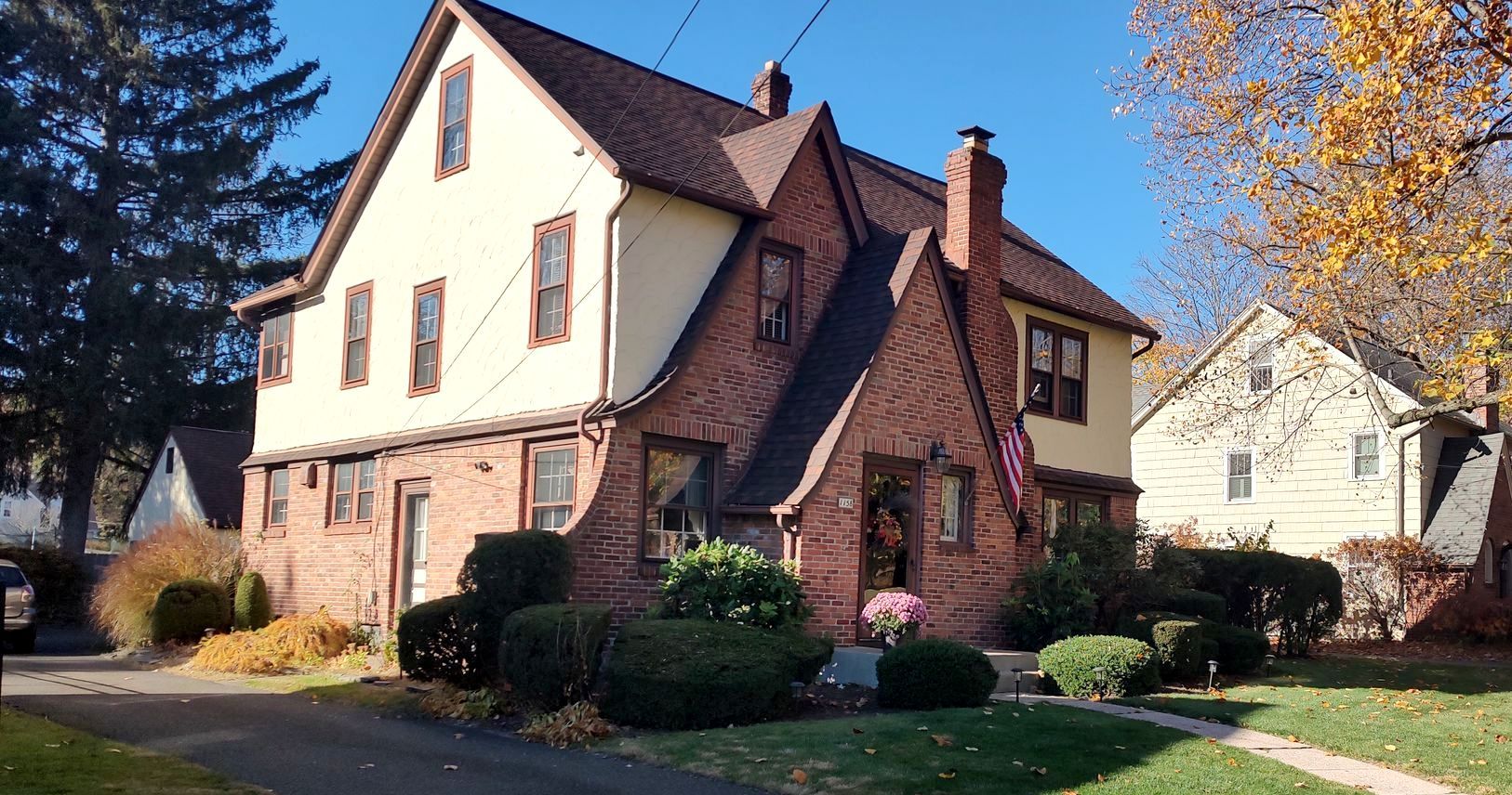 A large brick house with a red roof is surrounded by trees and bushes.