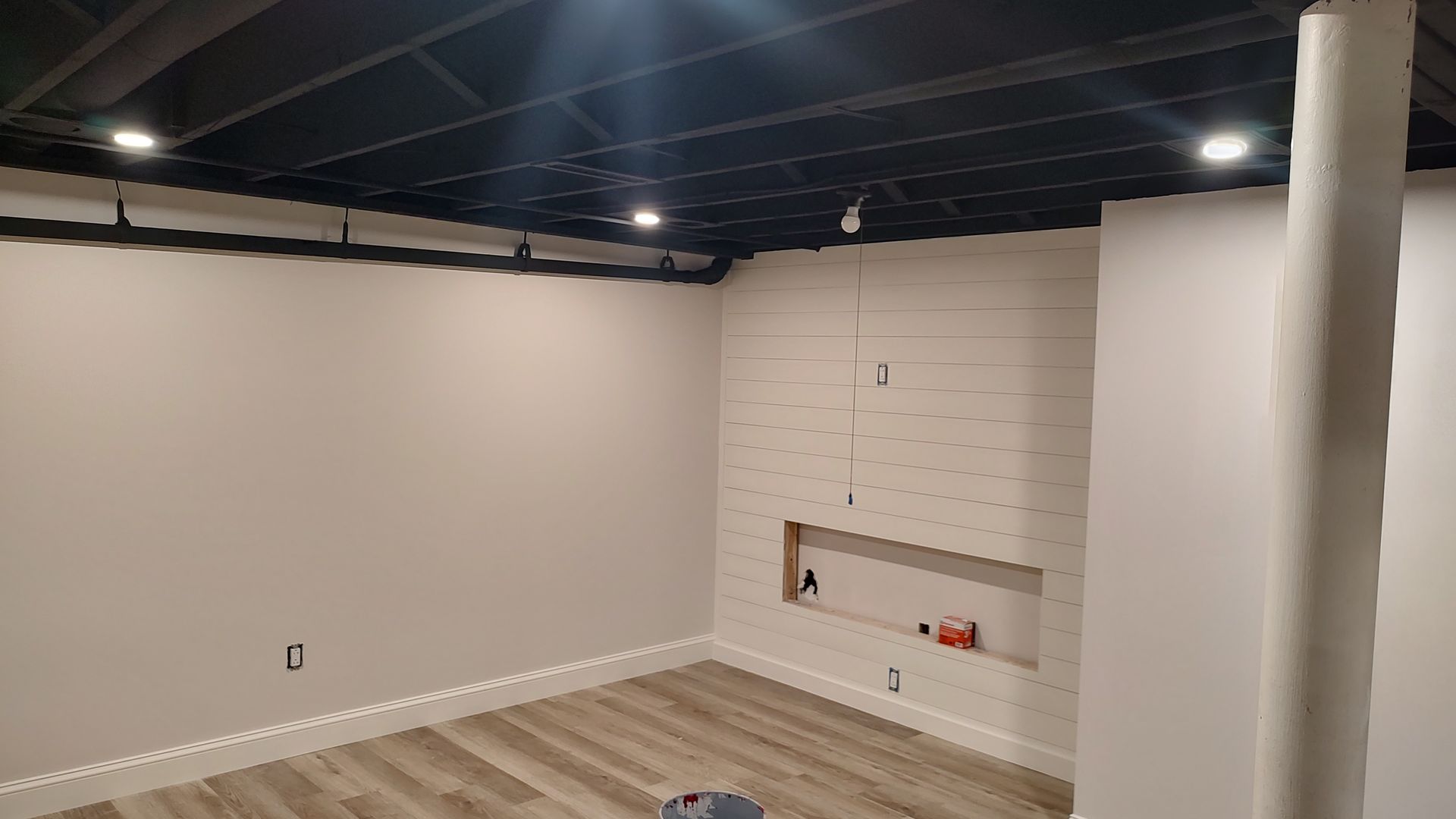 A basement with a black ceiling and white walls.
