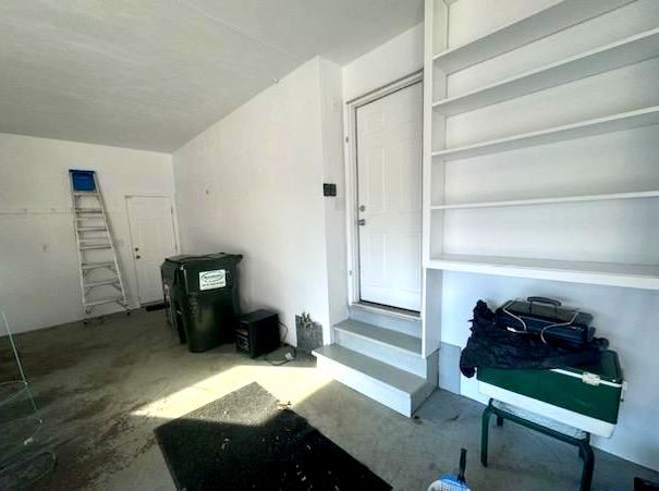 A garage with a trash can , stairs , shelves and a ladder.