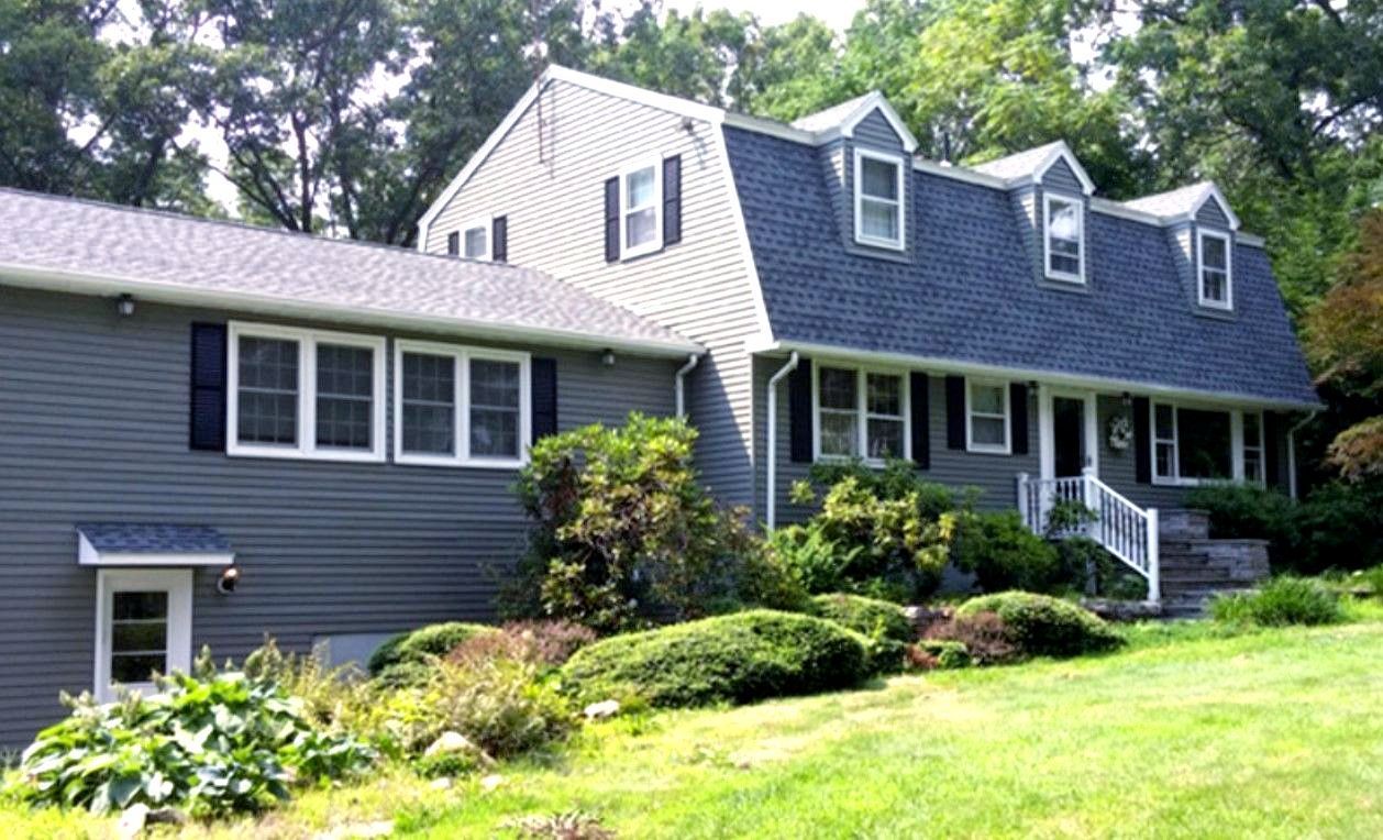 A large house with a blue roof is surrounded by trees and grass.