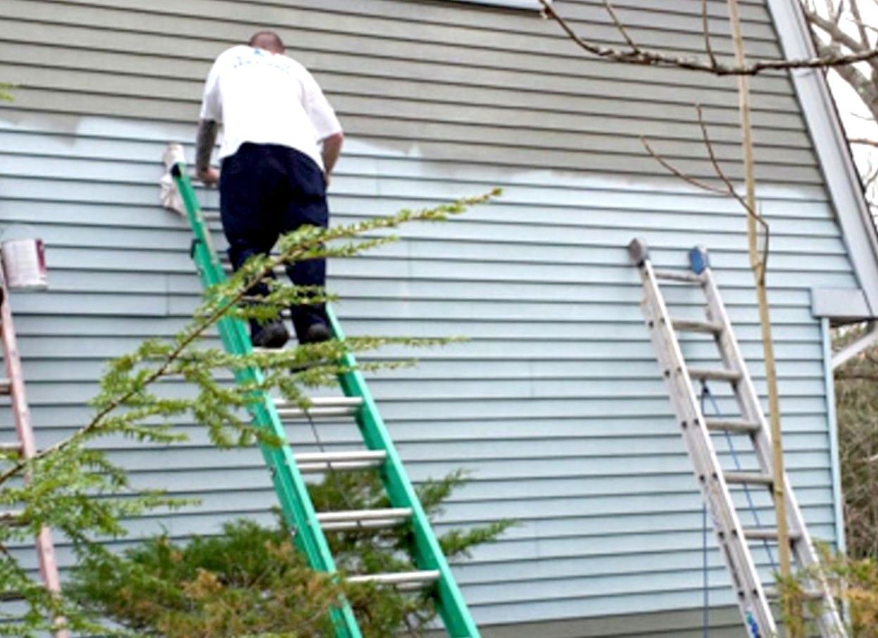 A man on a ladder paints the side of a house