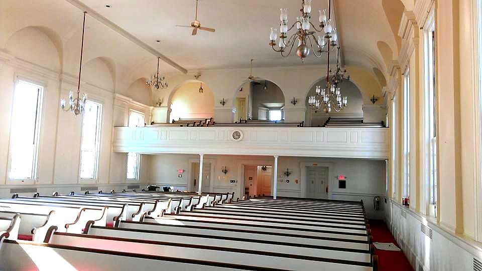 An empty church with rows of white benches and a balcony