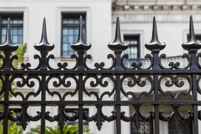 Black wrought iron fence in front of a white building with dark windows and a balcony.