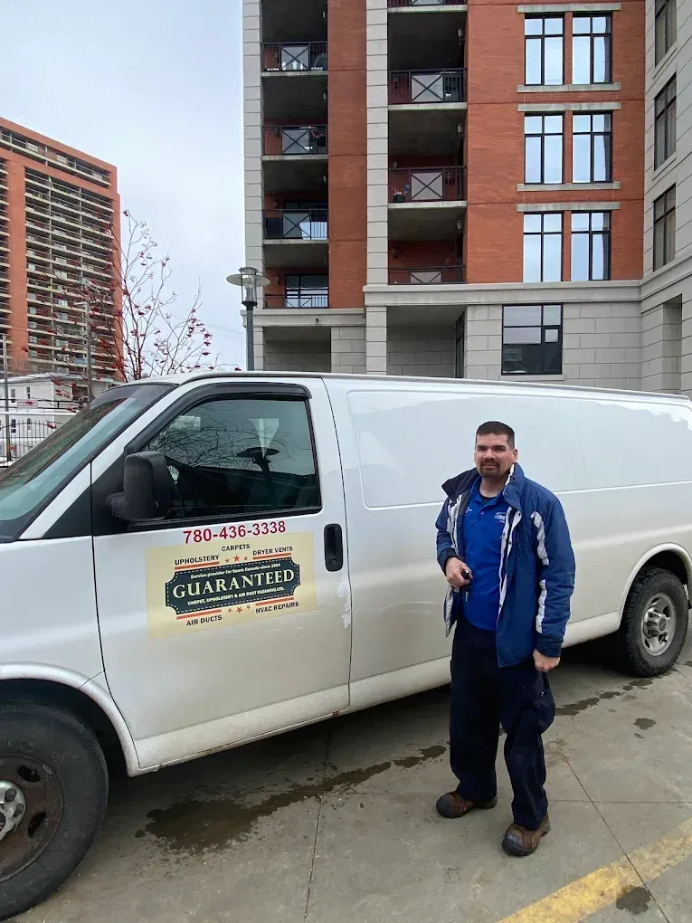 Man in blue jacket stands by a white van in front of a brick building. The van has 