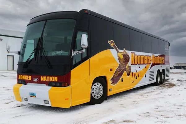 Yellow and black tour bus parked in a snowy lot with a dog graphic on the side