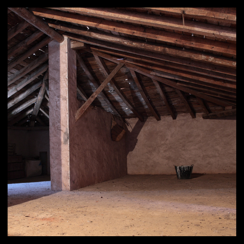 An empty room with wooden beams and a bucket on the floor