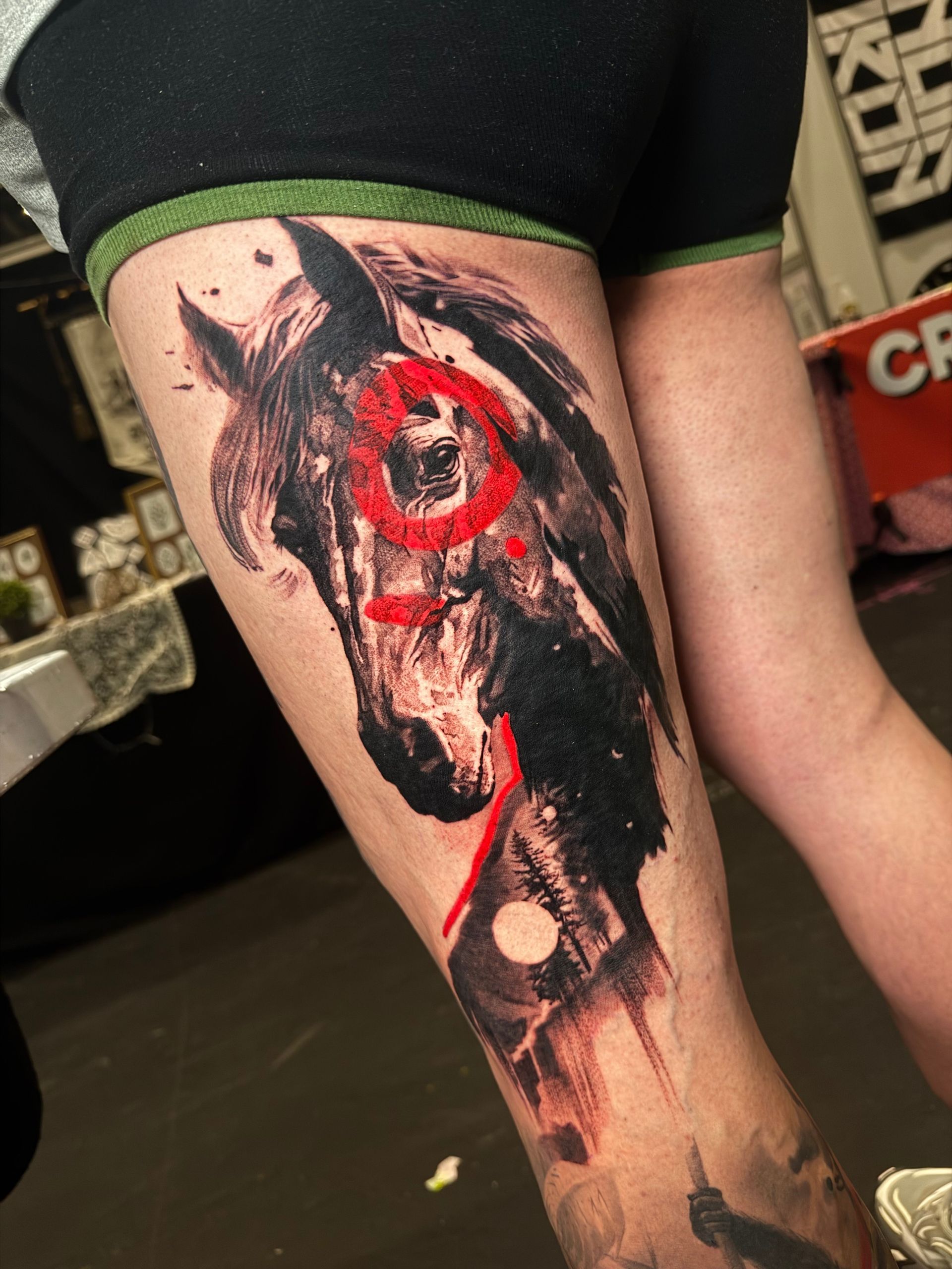 A thigh tattoo featuring a dark, painterly horse portrait accented with bold red abstract circles and brushstrokes.