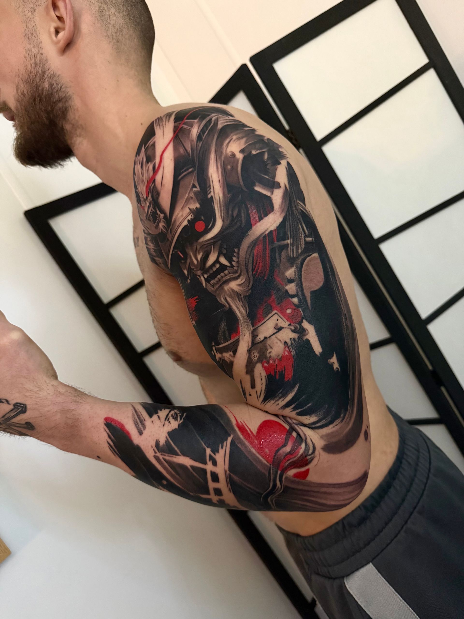 A person displays a detailed arm tattoo featuring a dark, stylized samurai mask with red eyes and flowing smoke motifs.