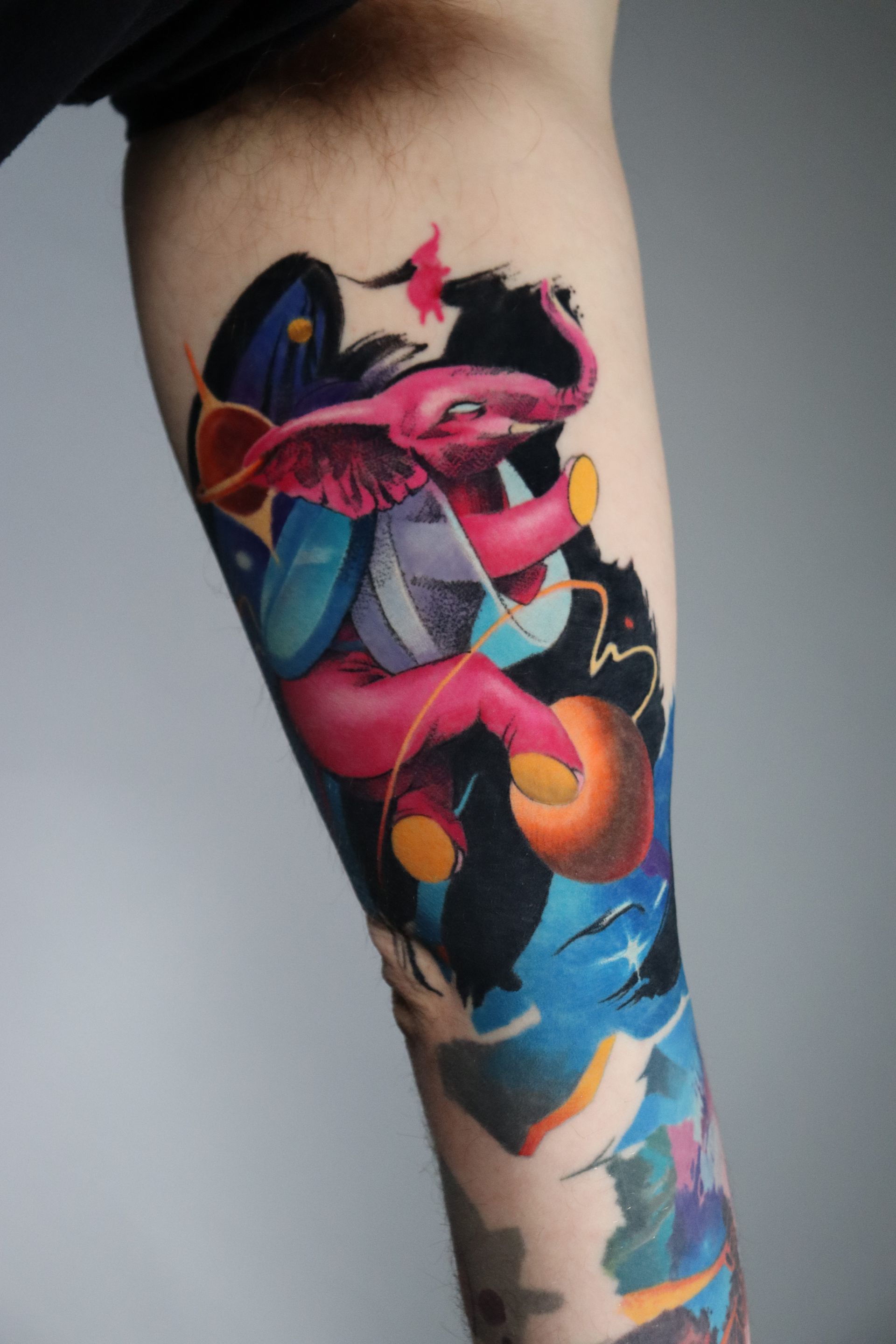 A colorful tattoo on an arm features a pink elephant with wings leaping through a dark, starry, cosmic background.