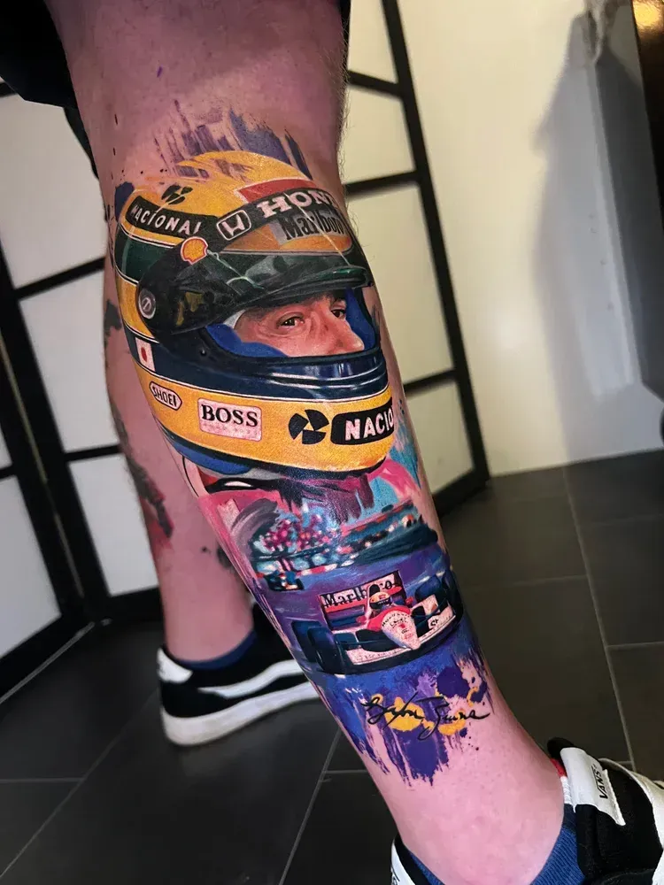 A detailed color tattoo on a lower leg featuring Ayrton Senna's iconic yellow racing helmet and his Formula 1 race car.
