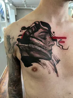 A chest tattoo featuring a profile portrait integrated with abstract black brushstrokes, geometric shapes, and red accents.