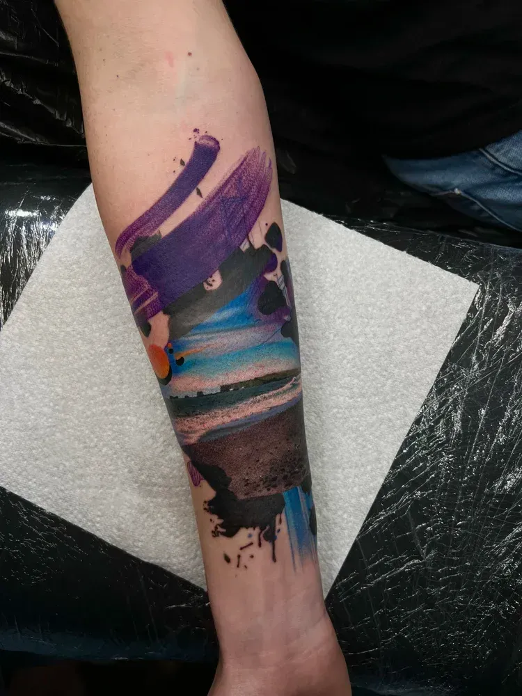 A forearm tattoo featuring a colorful landscape scene integrated with abstract, sweeping purple and black brushstrokes.