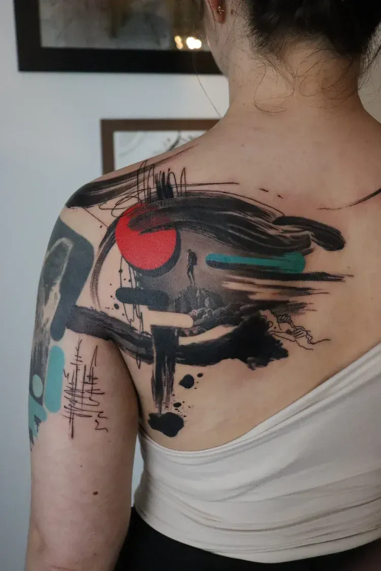 Abstract back and shoulder tattoo featuring bold black brushstrokes, a red circle, and teal accents on skin.