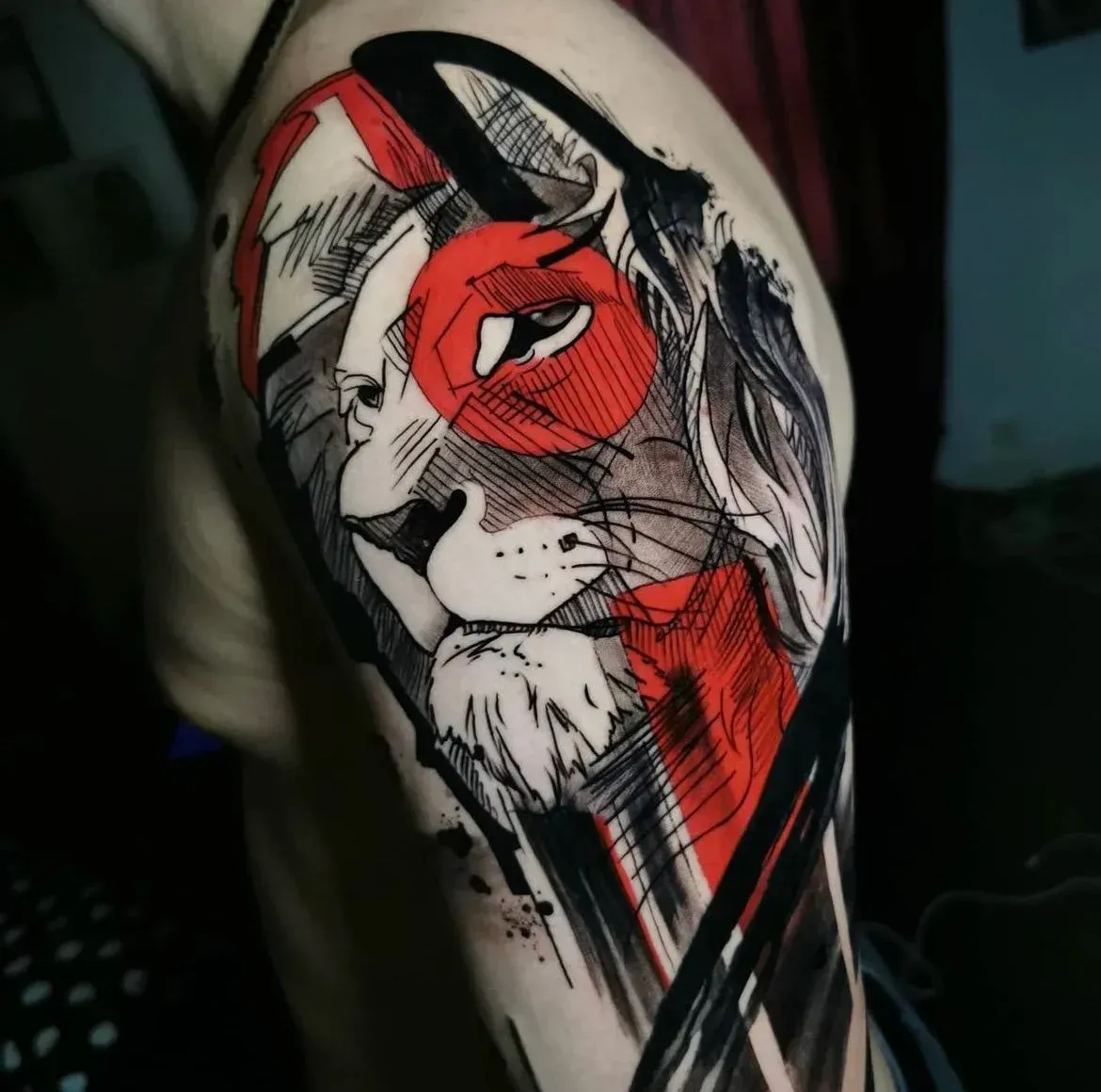 A stylized, graphic tattoo on a person's upper arm featuring a lion's head in black, white, and bold red geometric shapes.