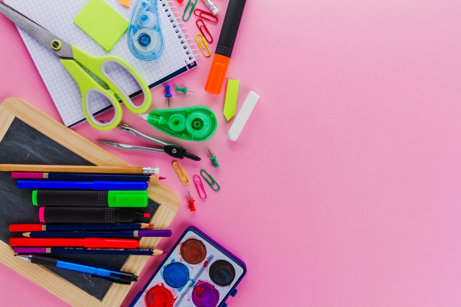 Artículos de papelería variados y coloridos esparcidos sobre un fondo rosa