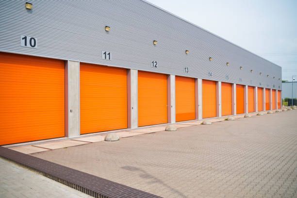 Row of orange storage unit doors numbered 10-17 in a long, gray building. The doors are framed in concrete.