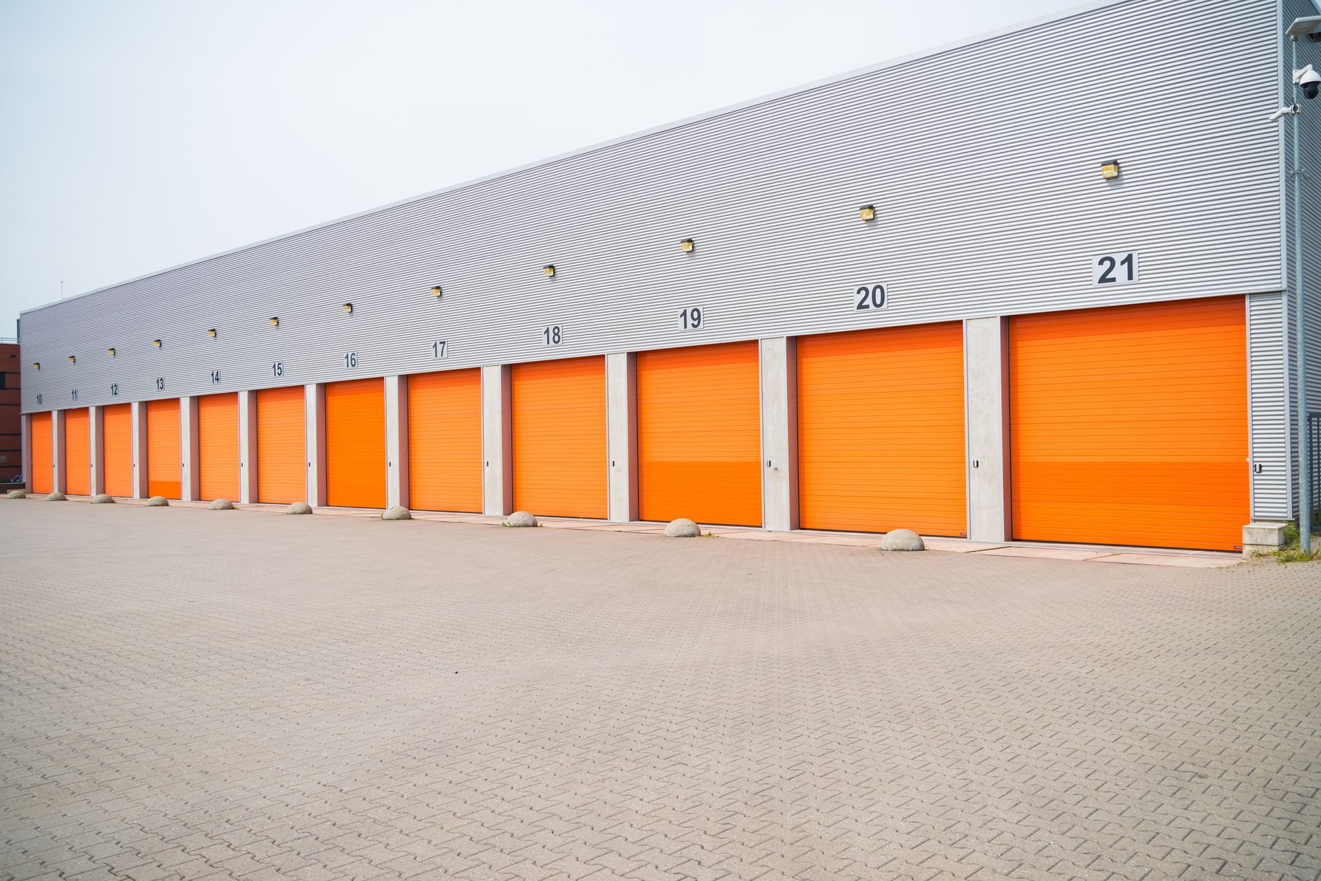 Row of orange storage unit doors in a building with a corrugated metal facade, set on a concrete lot.