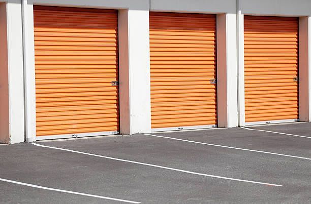 Three orange storage unit doors in a row, set in a row with white borders, against asphalt parking lot.