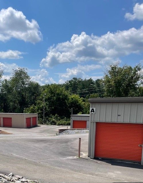 Storage units with orange doors, a blue sky, and green trees in the background.