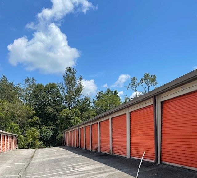 Row of orange storage units under a bright blue sky, with green trees and a concrete path.