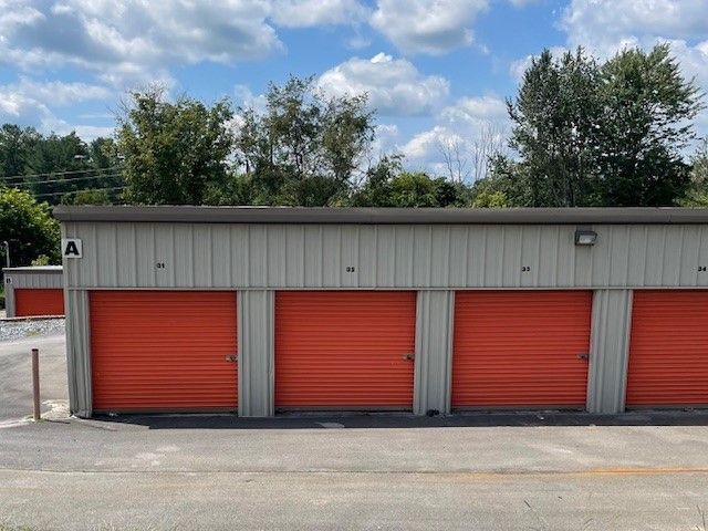 Row of orange storage unit doors under a tan roof with trees in the background.