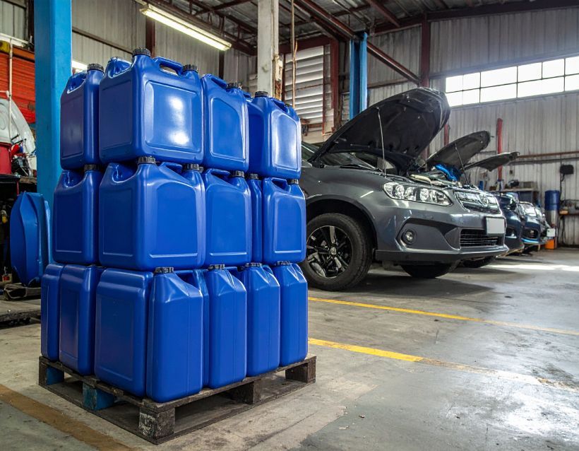 Blue oil containers stacked on a pallet in a car repair shop with vehicles.