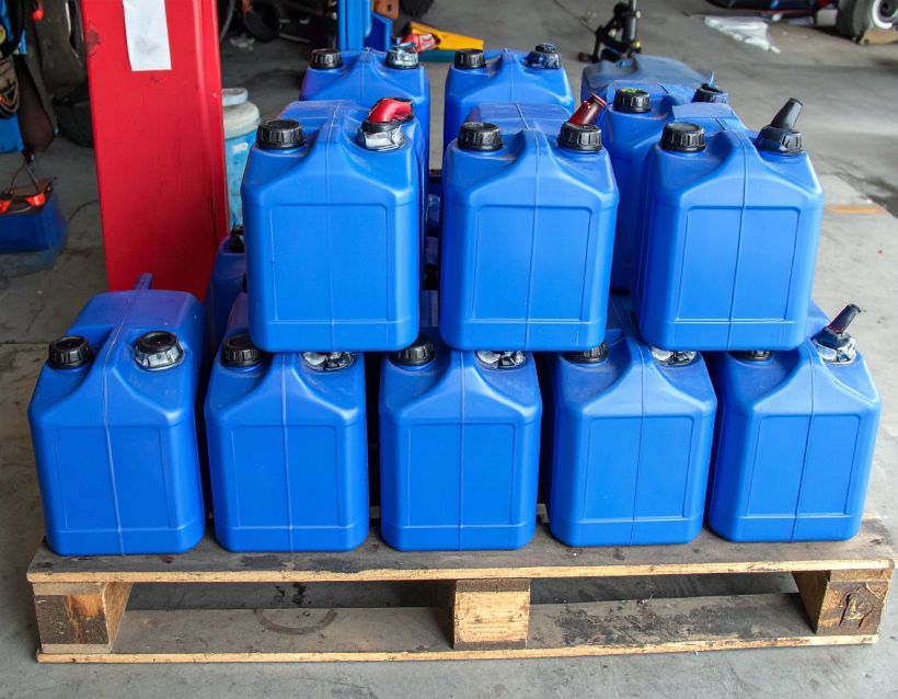 Blue plastic fuel containers stacked on a wooden pallet in a workshop setting.