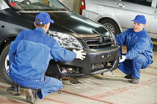 Two repairman mechanics matching an automobile body bumper in Norwich