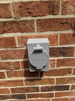 A brick wall with a gray electrical outlet on it.