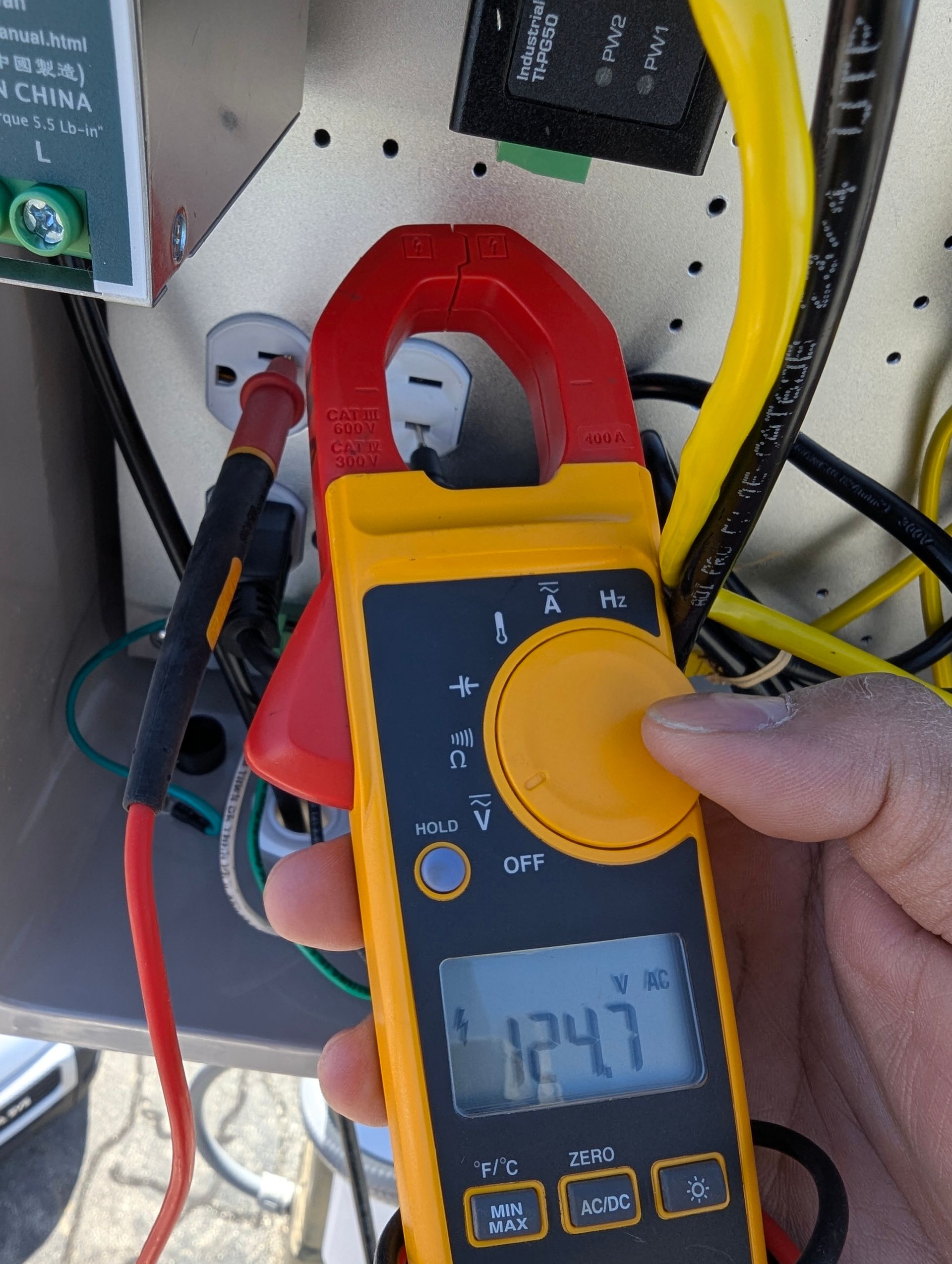 A hand is holding a clamp meter that reads 1241