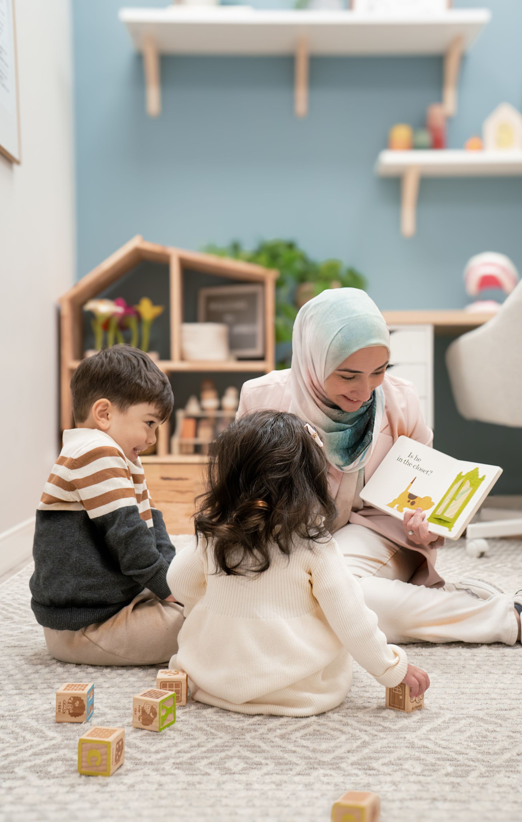 A woman is reading a book to two children while sitting on the floor.