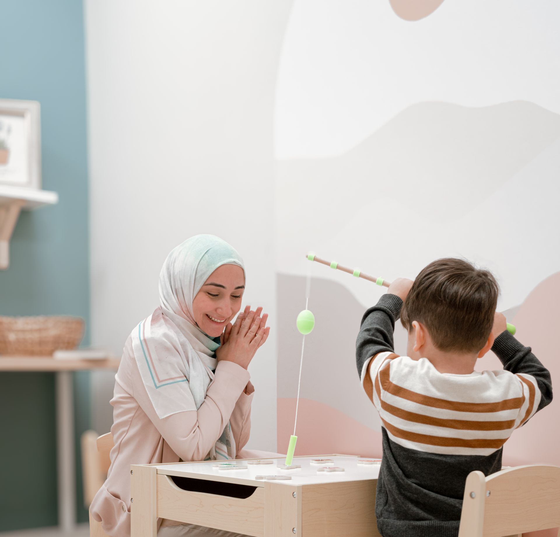 A woman is sitting at a table with a child playing with a toy.