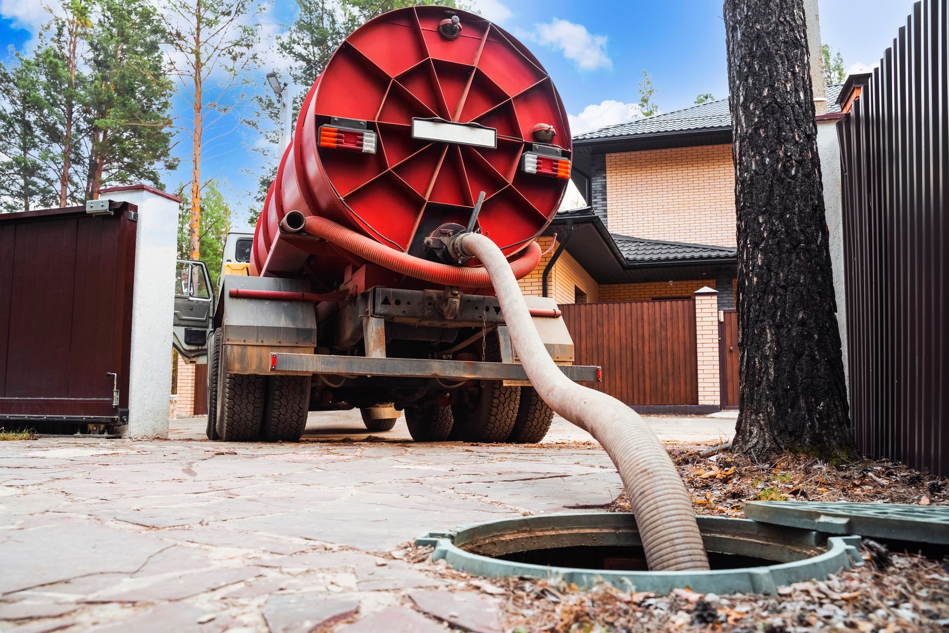 Red septic truck pumping waste from an underground tank in a driveway.