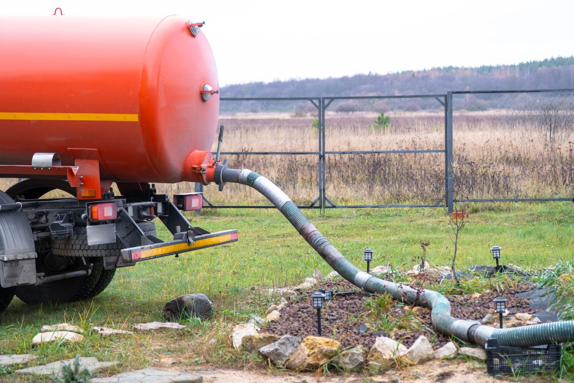 A red septic truck with a hose connected, pumping liquid from an underground septic tank outdoors A red septic truck with a hose connected, pumping liquid from an underground septic tank outdoors