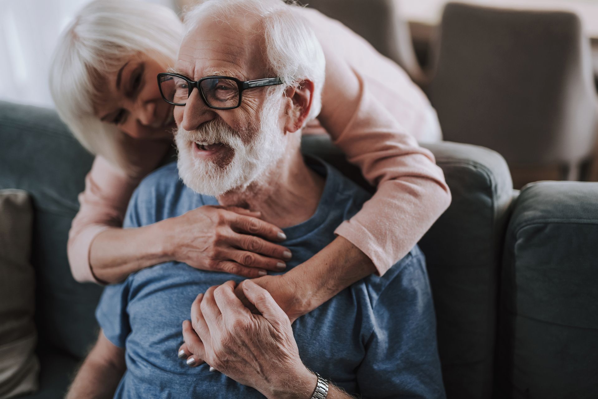Elderly couple embracing on a couch, with the woman resting her head on the man’s shoulder