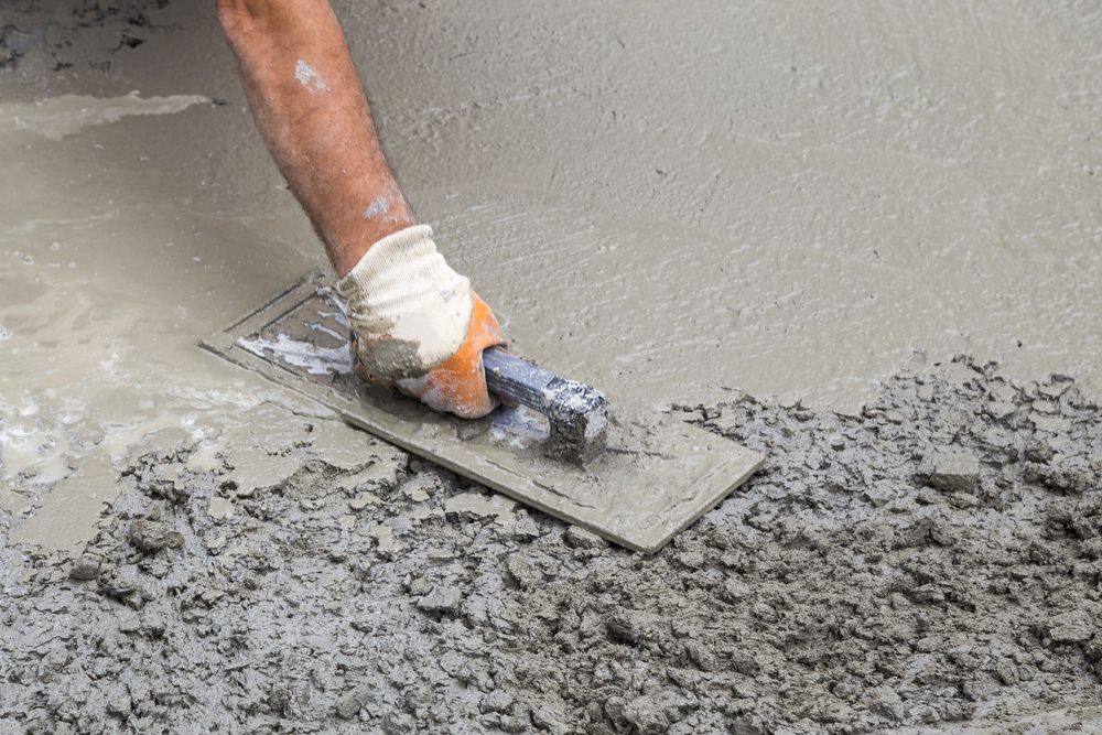 Gloved hand smoothing wet concrete with a trowel on a fresh slab