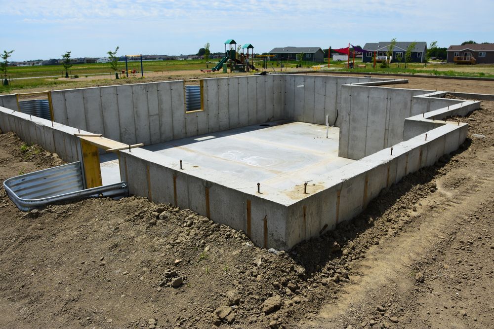 Concrete foundation under construction on a dirt lot, with a flat slab and low walls.