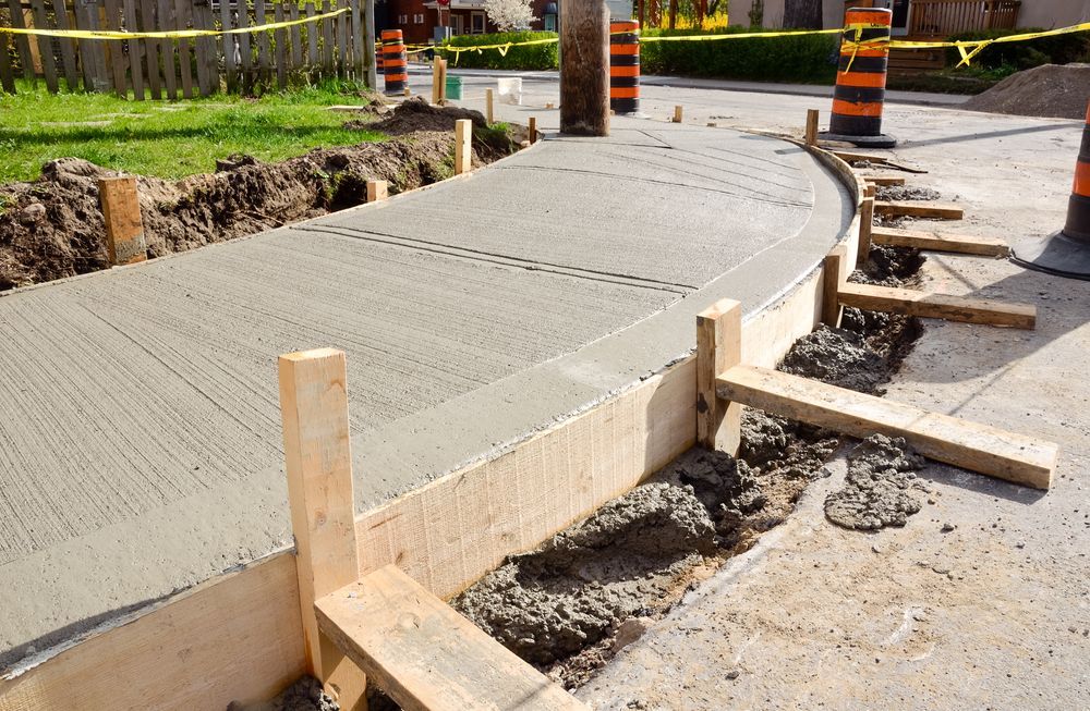 Freshly poured concrete sidewalk curve with wooden forms and orange traffic barrels at a construction site